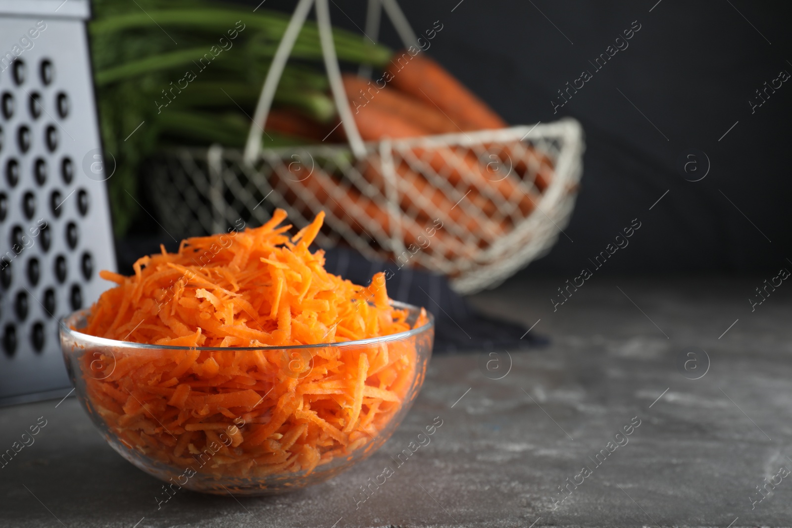 Photo of Glass bowl with grated carrot on grey table, closeup