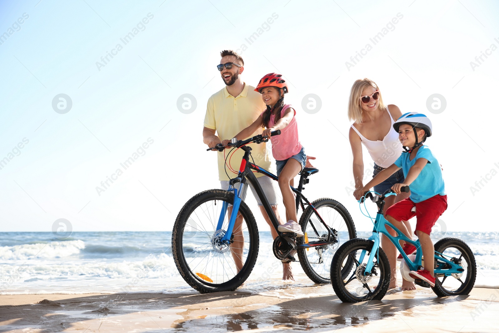 Photo of Happy parents teaching children to ride bicycles on sandy beach near sea