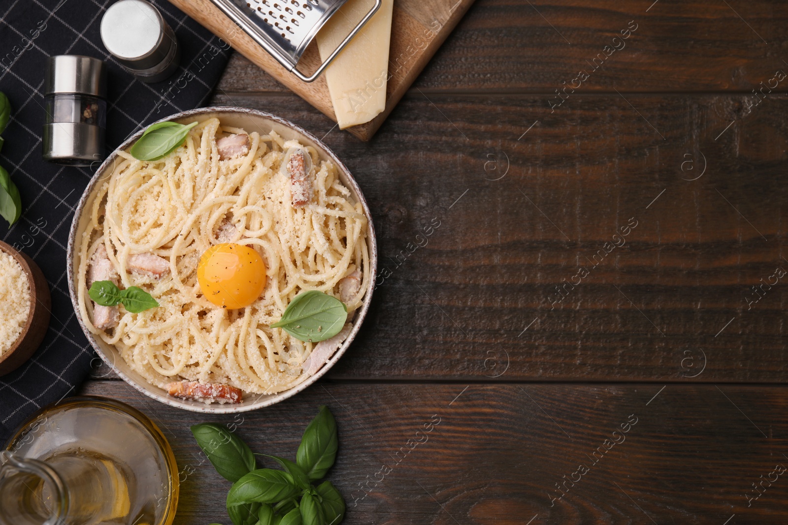 Photo of Bowl of tasty pasta Carbonara with basil leaves and egg yolk on wooden table, flat lay. Space for text