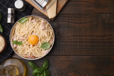 Bowl of tasty pasta Carbonara with basil leaves and egg yolk on wooden table, flat lay. Space for text