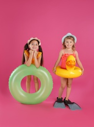 Cute little children in beachwear with bright inflatable rings on pink background