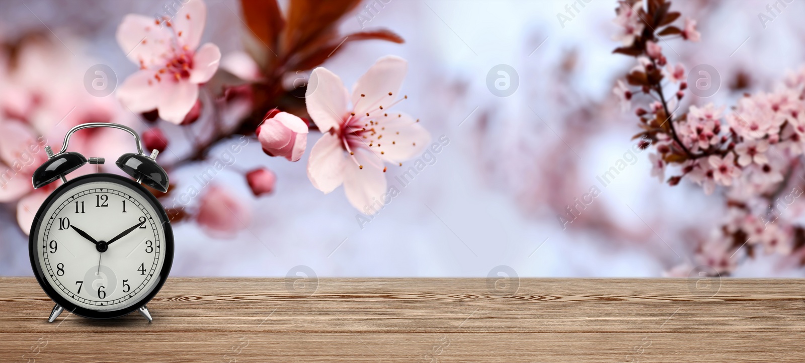 Image of Black alarm clock on wooden table, space for text. Daylight saving time (Spring forward)