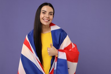 Photo of Happy young woman with flag of United Kingdom showing thumbs up on violet background