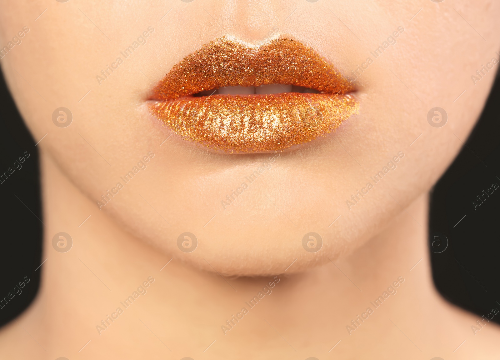 Photo of Beautiful young model with golden lips makeup on black background