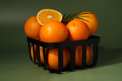 Fresh oranges in metal basket on green background, closeup