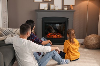 Photo of Happy family spending time together near fireplace at home, back view