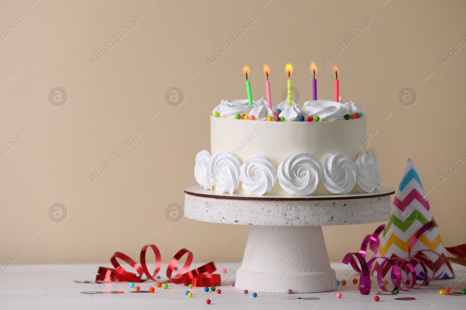 Photo of Delicious birthday cake and party decor on white wooden table against beige background, space for text