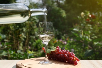 Photo of Pouring white wine from bottle into glass at wooden table outdoors, closeup. Space for text