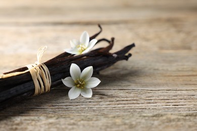 Photo of Bunch of vanilla pods and flowers on wooden table, closeup. Space for text