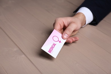 Man holding medical business card at wooden table, closeup. Women's health service