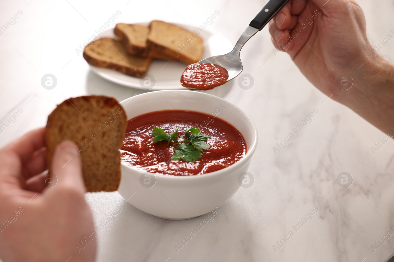Photo of Man eating delicious tomato soup at light marble table, closeup