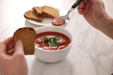 Man eating delicious tomato soup at light marble table, closeup