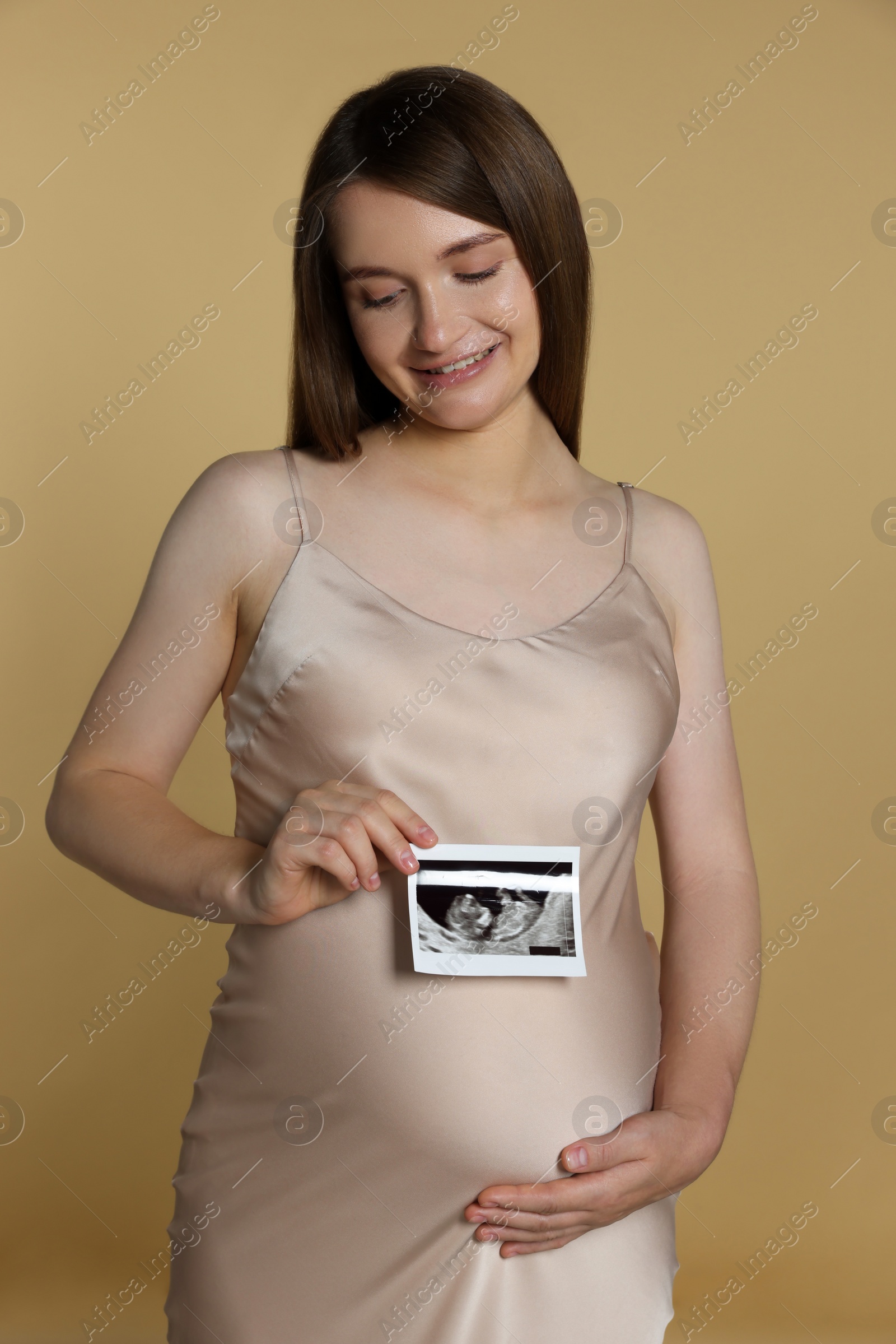 Photo of Pregnant woman with ultrasound picture of baby on beige background