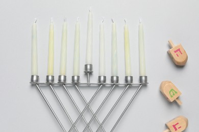 Photo of Hanukkah menorah with candles and dreidel on light background, flat lay