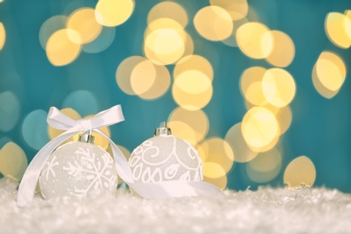 Beautiful white Christmas balls on snow against blurred festive lights, space for text