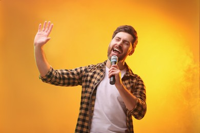 Photo of Handsome man with microphone singing on golden background