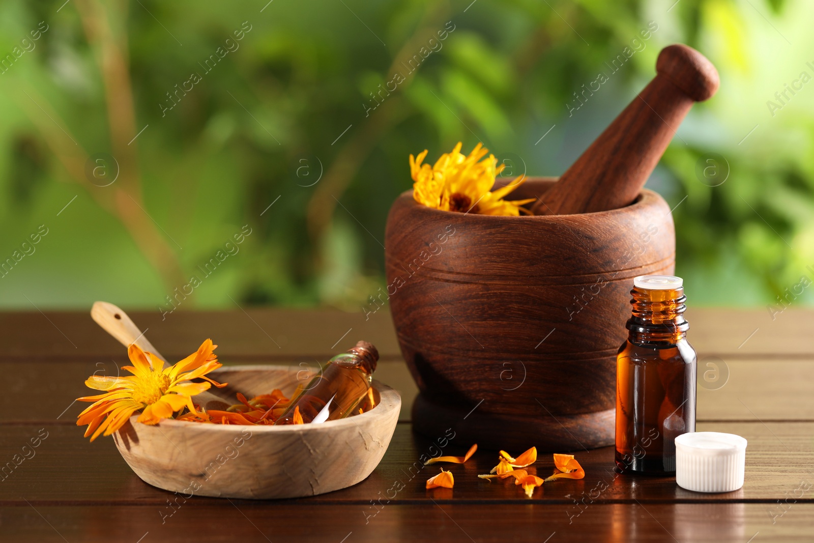 Photo of Bottles of essential oils, mortar and beautiful calendula flowers on wooden table outdoors