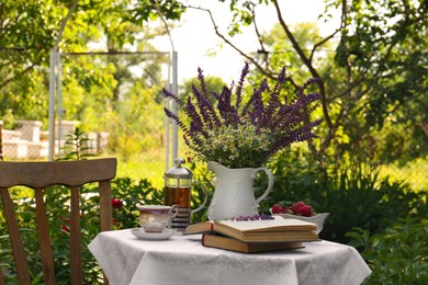 Photo of Beautiful bouquet of wildflowers and books on table served for tea drinking in garden