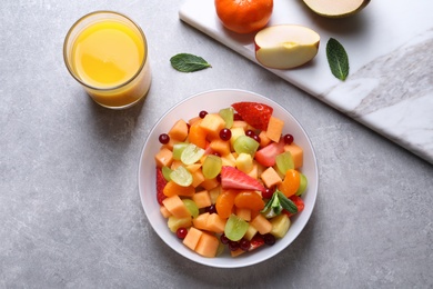 Photo of Bowl with fresh fruit salad and glass of juice on grey background