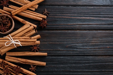 Aromatic cinnamon sticks and anise on black wooden table, flat lay. Space for text