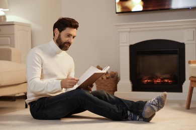 Handsome man reading book near fireplace in room