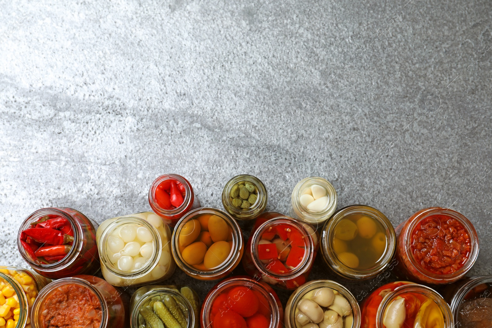 Photo of Flat lay composition with jars of pickled vegetables on grey table. Space for text