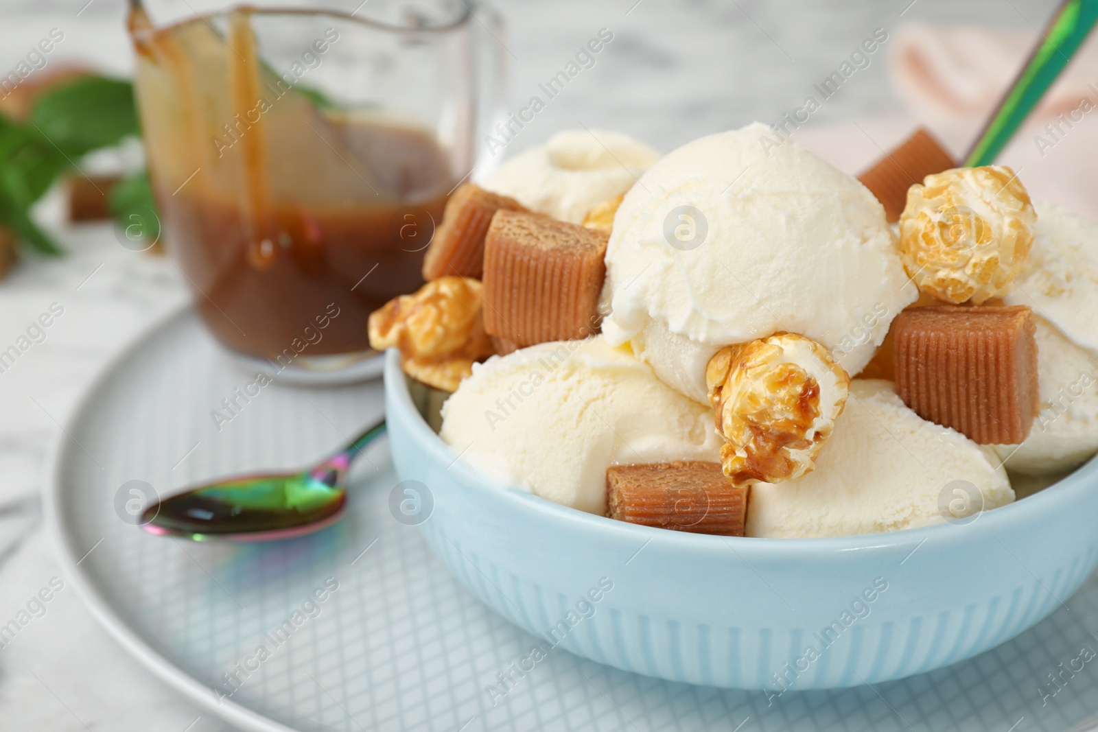 Photo of Plate of delicious ice cream with caramel candies and popcorn on table, closeup