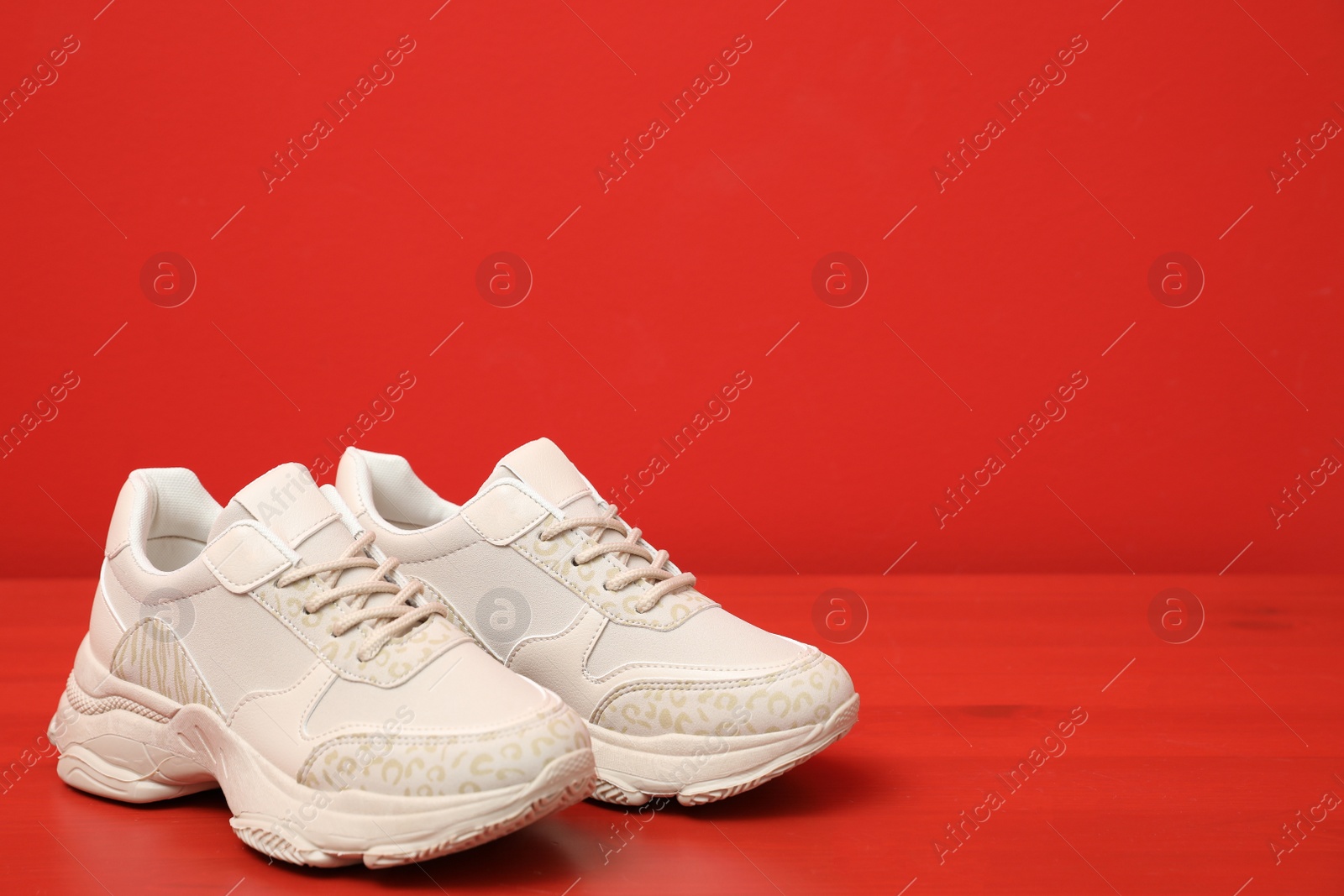 Photo of Stylish women's sneakers on wooden table near red wall, space for text