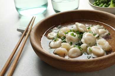 Photo of Plate of tasty dumplings in broth with chopsticks on grey table, closeup