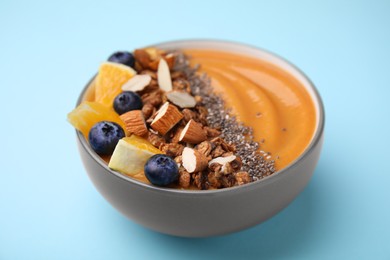 Bowl of delicious fruit smoothie with fresh orange slices, blueberries and granola on light blue background, closeup