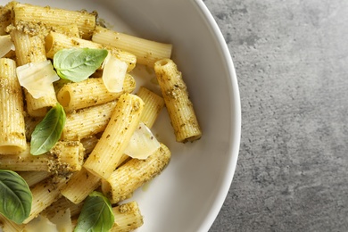 Plate with delicious basil pesto pasta on gray table, top view