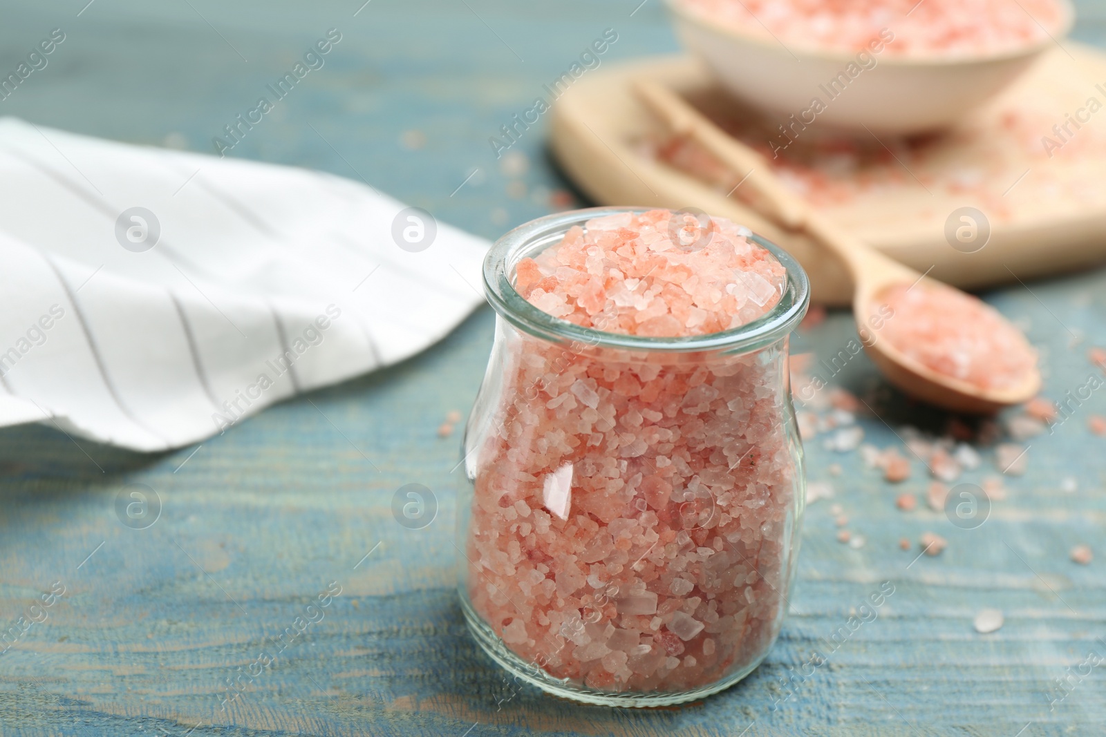 Photo of Jar with pink himalayan salt on light blue wooden table, closeup