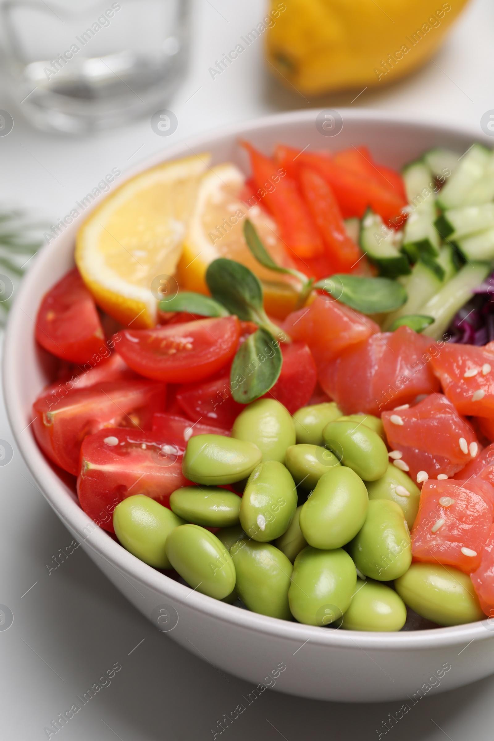 Photo of Poke bowl with salmon, edamame beans and vegetables on white table, closeup