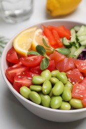 Poke bowl with salmon, edamame beans and vegetables on white table, closeup