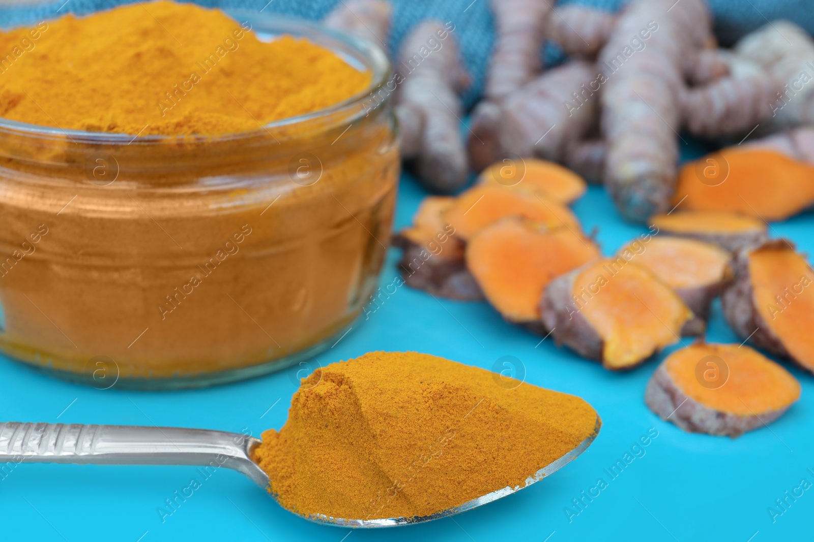 Photo of Glass jar of turmeric powder and roots on light blue tray, closeup