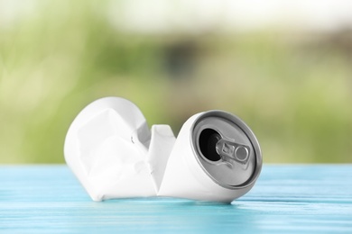 Crumpled aluminum can on table against blurred background. Metal waste recycling