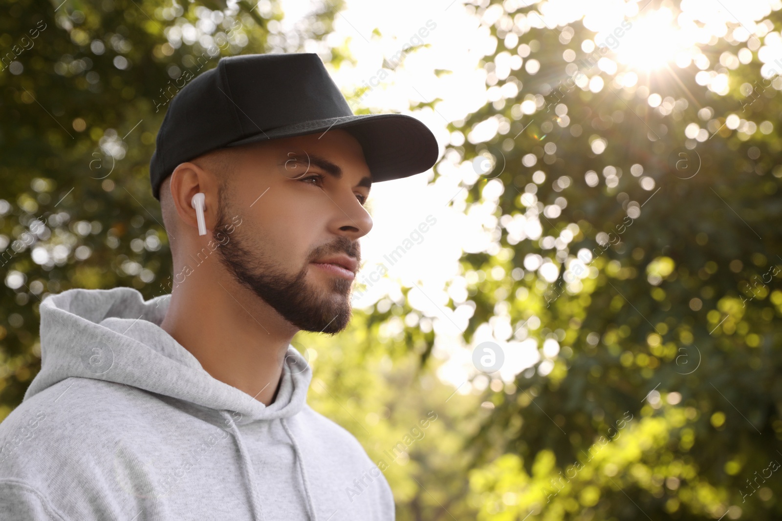 Photo of Young man with wireless headphones listening to music in park. Space for text