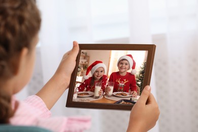 Image of Little girl holding frame with photo portrait of her family indoors, closeup