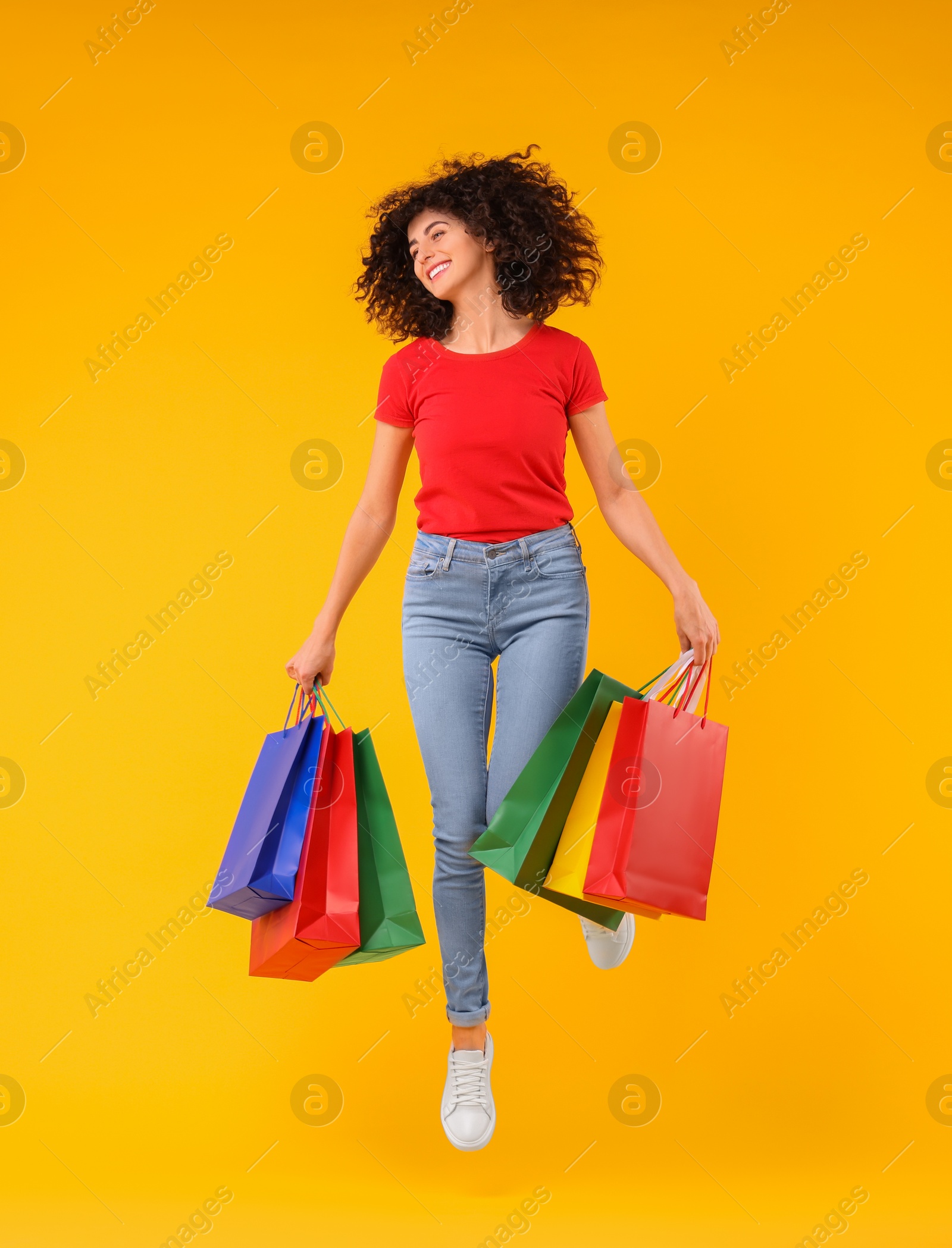 Photo of Happy young woman with shopping bags on yellow background. Space for text