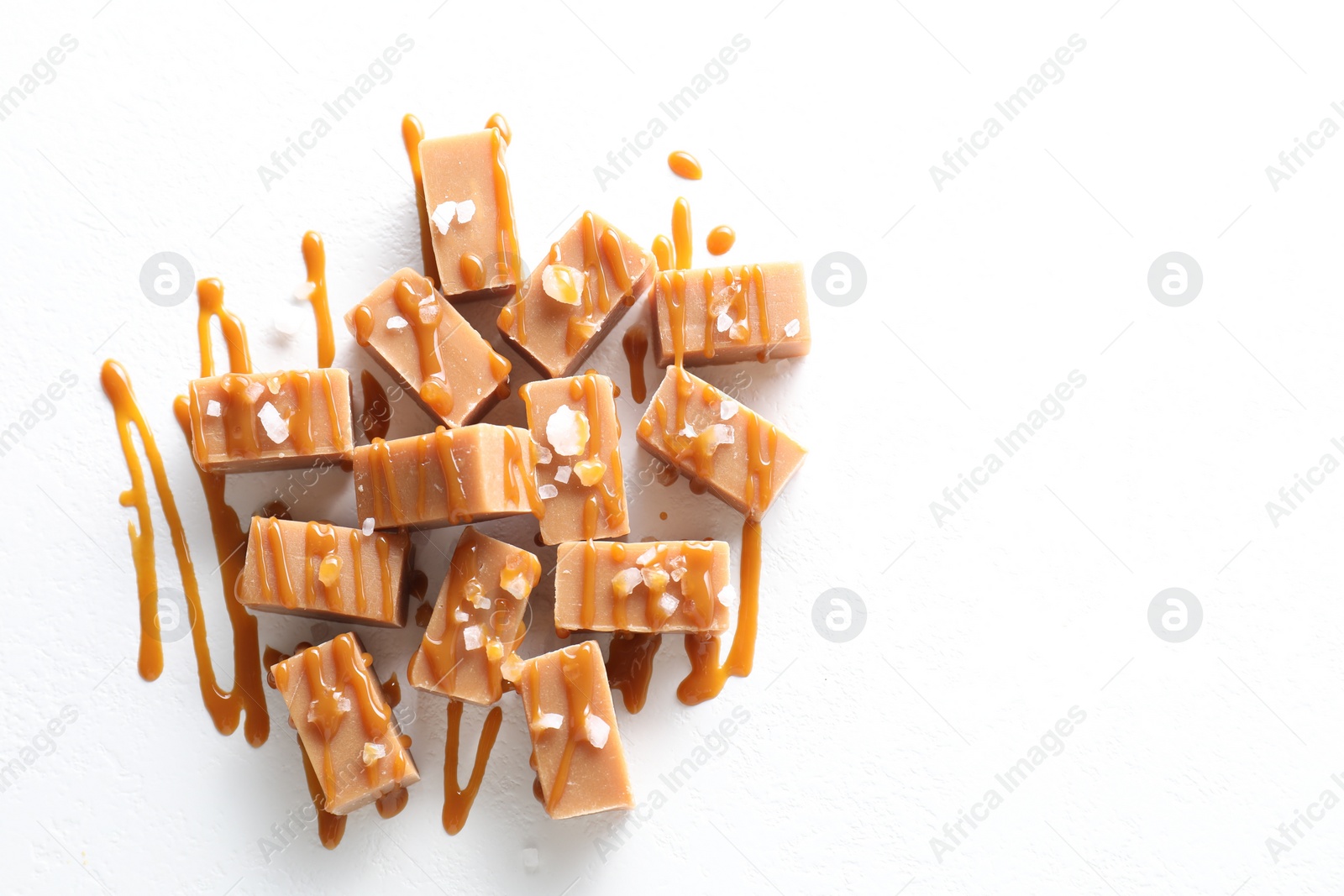 Photo of Tasty candies, caramel sauce and salt on white table, top view. Space for text