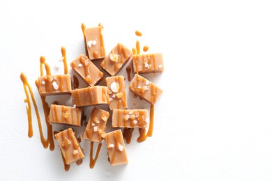 Photo of Tasty candies, caramel sauce and salt on white table, top view. Space for text