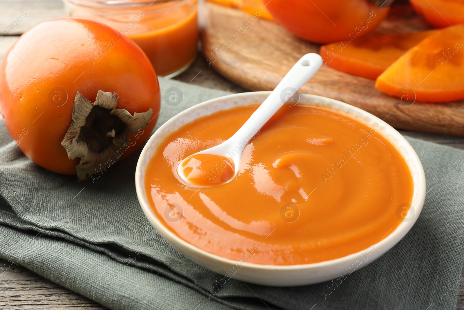 Photo of Delicious persimmon jam and fresh fruits on wooden table, closeup