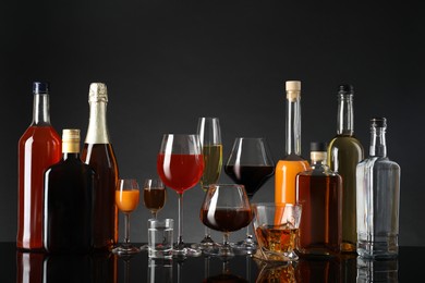 Bottles and glasses with different alcoholic drinks on table against gray background