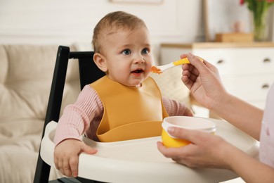 Photo of Mother feeding her little baby at home. Kid wearing silicone bib