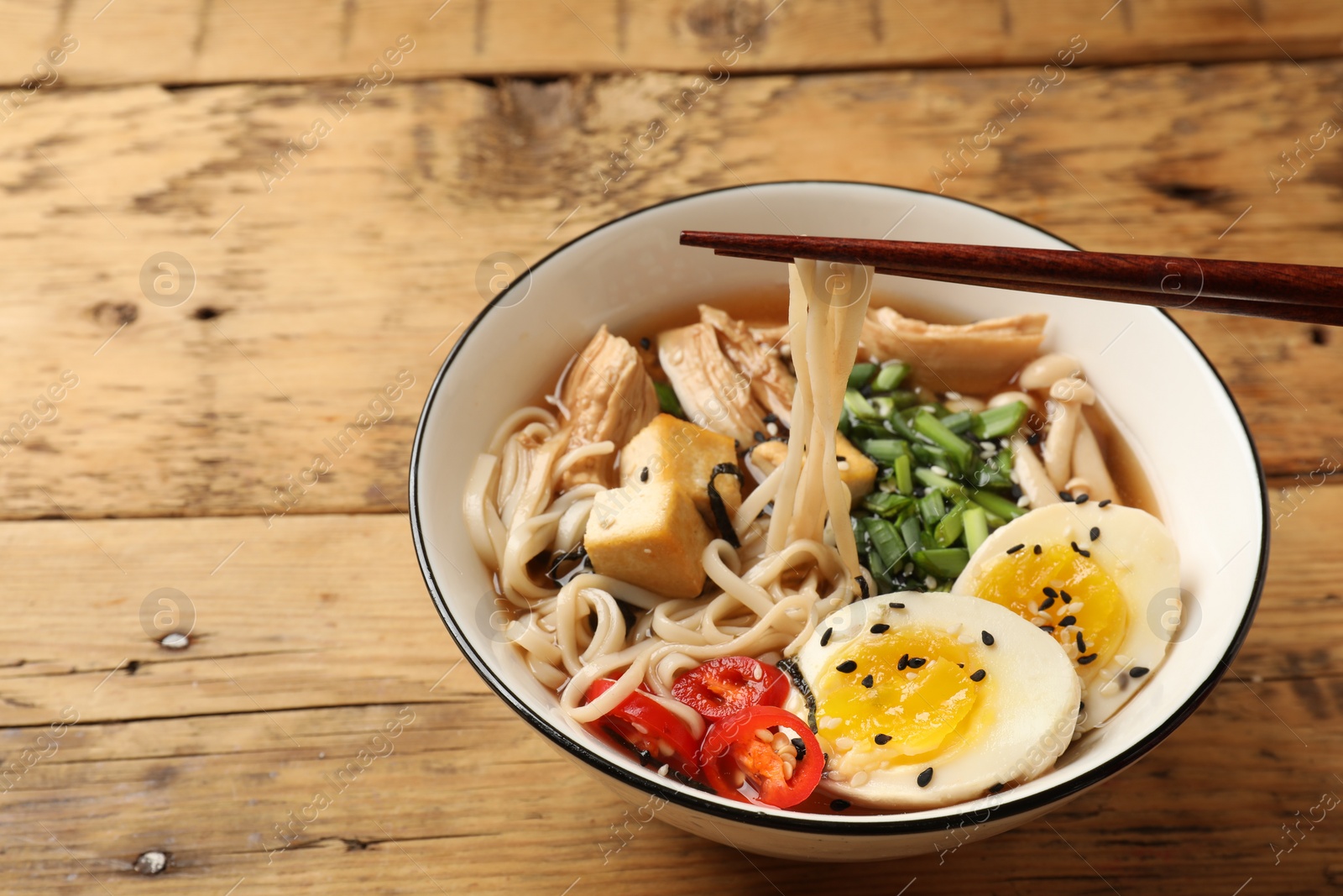 Photo of Noodle soup. Eating delicious ramen with chopsticks on wooden table, closeup. Space for text