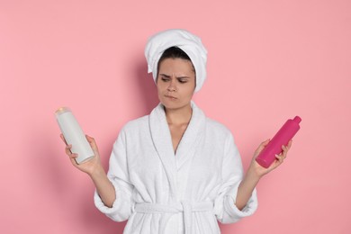 Beautiful young woman holding bottles of shampoo on pink background