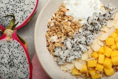 Bowl of granola with pitahaya, mango and yogurt on light grey table, flat lay