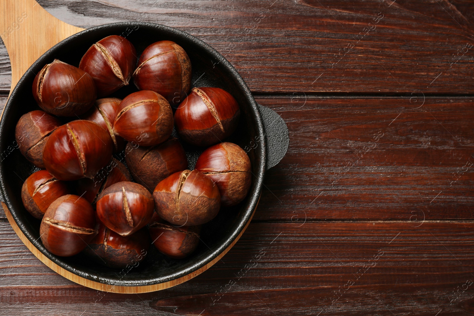 Photo of Roasted edible sweet chestnuts in baking dish on wooden table, top view. Space for text