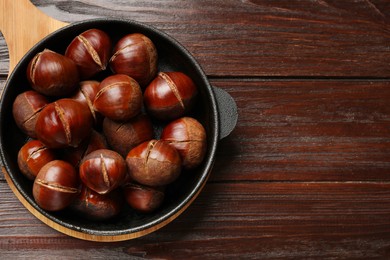 Roasted edible sweet chestnuts in baking dish on wooden table, top view. Space for text