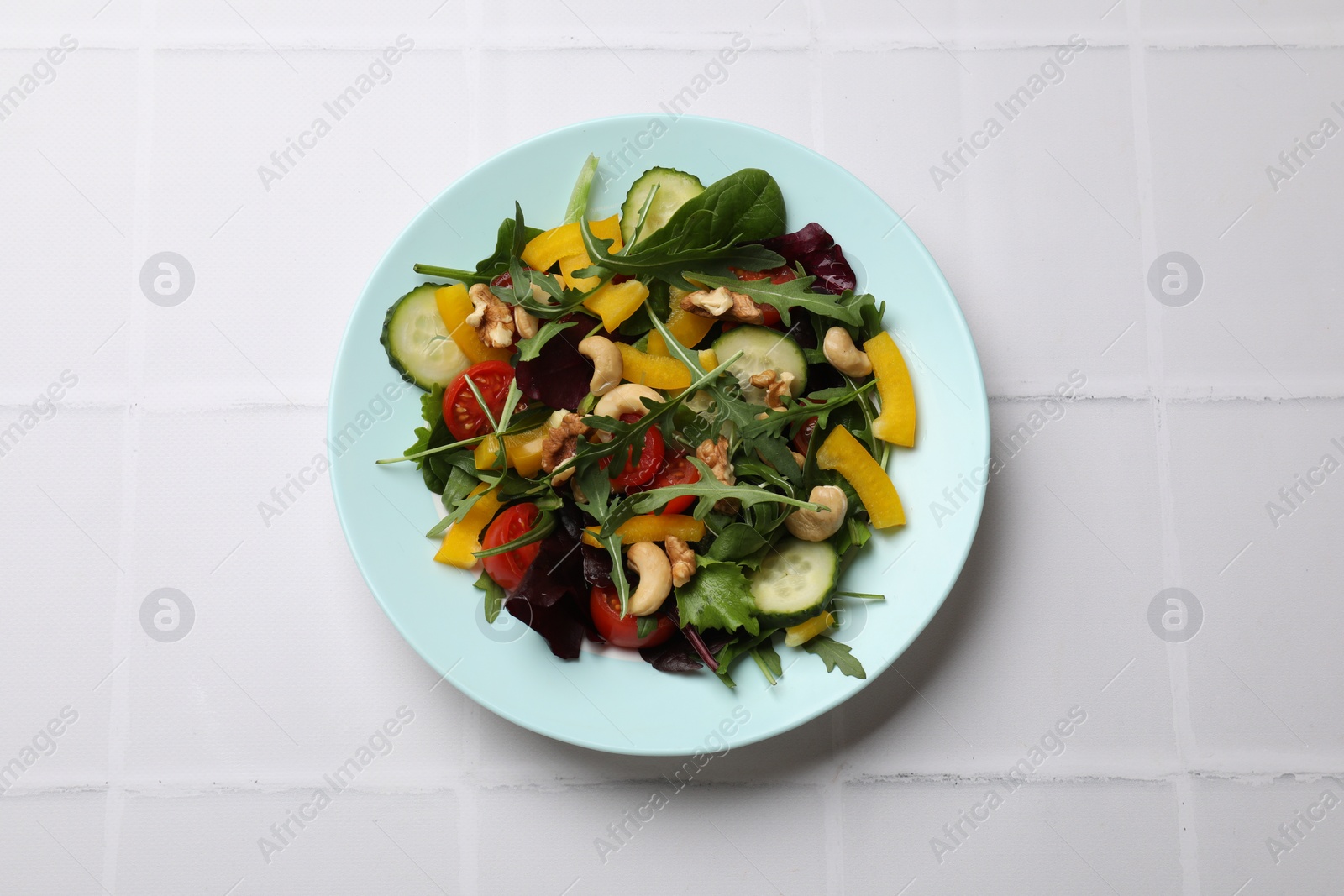 Photo of Tasty fresh vegetarian salad on white tiled table, top view